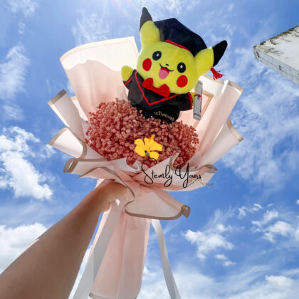 Graduation bouquet featuring a Pikachu plushie and pink preserved flowers under a bright blue sky – Stemly Yours Singapore.